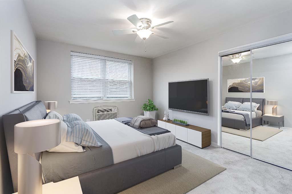 Light grey walls & carpet in bedroom. Mirror closet doors, mounted TV, & window. With A/C unit & fan